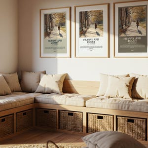 K&ouml;nnte beinhalten: Drei gerahmte Poster mit dem Text "Franny and Zooey" h&auml;ngen &uuml;ber einer eingebauten Bank mit beigen Kissen und Polstern. Die Bank hat gewebte Aufbewahrungsk&ouml;rbe. Ein gro&szlig;es Fenster und eine dekorative Pflanze sind ebenfalls sichtbar.