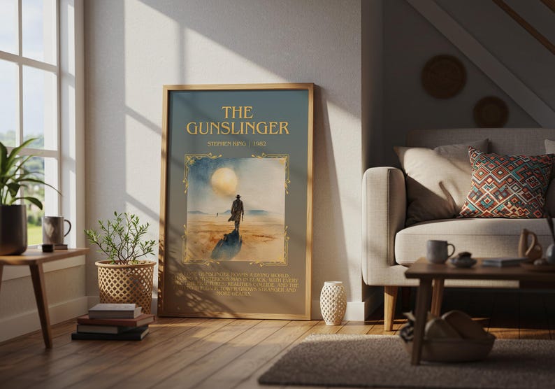 May include: Framed poster of "The Gunslinger" by Stephen King. The artwork depicts a lone figure in a desert landscape under a large moon. The poster is in a wooden frame and is displayed in a living room setting.