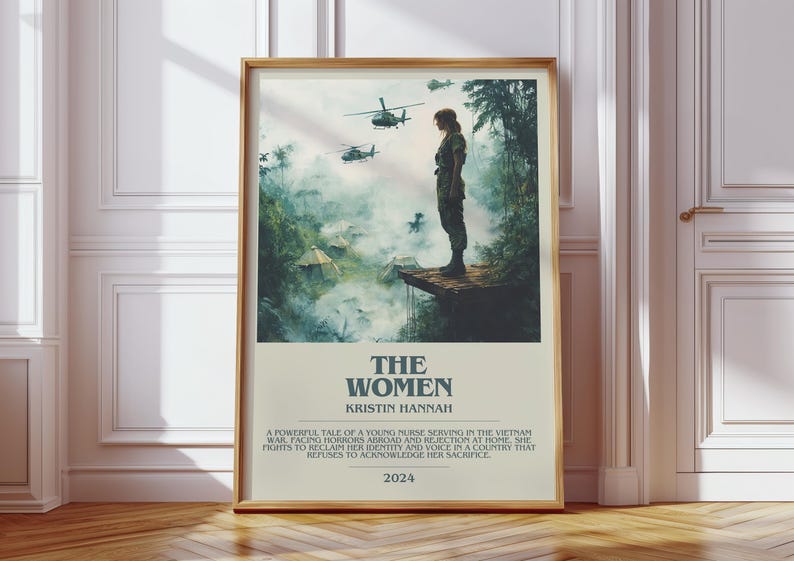 Puede incluir: Un p&oacute;ster enmarcado con el t&iacute;tulo "THE WOMEN" de Kristin Hannah. La imagen muestra a una mujer con uniforme militar de pie en una plataforma de madera, con helic&oacute;pteros al fondo. El p&oacute;ster est&aacute; sobre un suelo de madera.