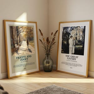 K&ouml;nnte beinhalten: Zwei gerahmte Kunstdrucke, "Franny and Zooey" und "The Great Gatsby", lehnen an einer Wand. Der "Franny and Zooey" Druck zeigt eine Person, die auf einem Weg geht. Der "Great Gatsby" Druck zeigt ein Paar vor einem Geb&auml;ude. Eine Vase mit getrockneten Pflanzen steht dazwischen.