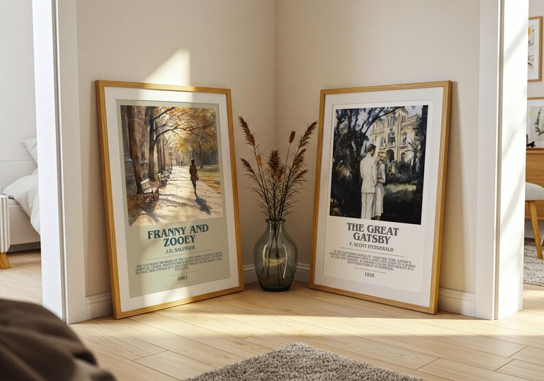 K&ouml;nnte beinhalten: Zwei gerahmte Kunstdrucke, "Franny and Zooey" und "The Great Gatsby", lehnen an einer Wand. Der "Franny and Zooey" Druck zeigt eine Person, die auf einem Weg geht. Der "Great Gatsby" Druck zeigt ein Paar vor einem Geb&auml;ude. Eine Vase mit getrockneten Pflanzen steht dazwischen.