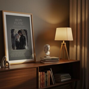 May include: A framed print with the text "IRON FLAME" and an image of two people. The print is displayed on a wooden cabinet with a lamp and decorative busts. A stack of books and a wooden sculpture are also on the cabinet.