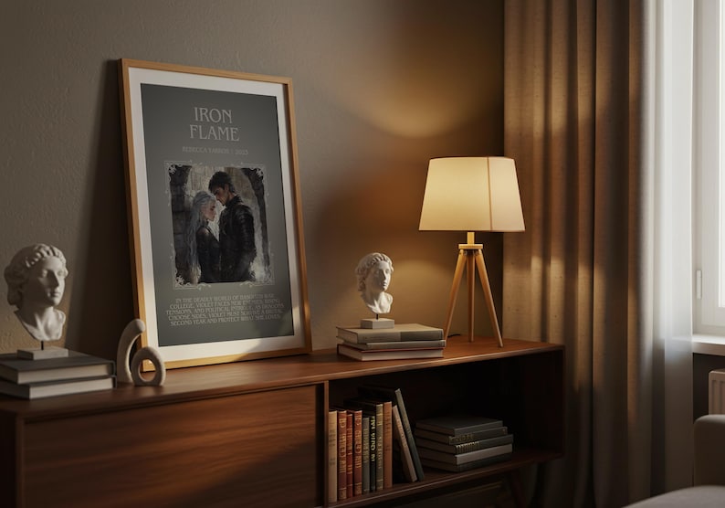 May include: A framed print with the text "IRON FLAME" and an image of two people. The print is displayed on a wooden cabinet with a lamp and decorative busts. A stack of books and a wooden sculpture are also on the cabinet.