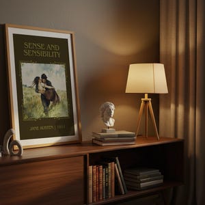 May include: A framed print of "Sense and Sensibility" by Jane Austen, displayed on a wooden cabinet. The print features a romantic illustration. A lamp with a beige shade and a bust sculpture are also on the cabinet.