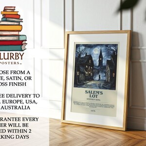 May include: A framed poster featuring a nighttime scene of a town with a church steeple under a full moon. The poster is titled "Salem's Lot" by Stephen King. The poster is in a wooden frame and is displayed on a wooden floor.