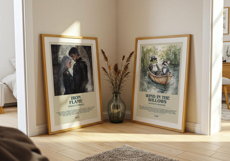 May include: Two framed art prints leaning against a wall. One features a couple with the text "Iron Flame" and the other depicts a frog and a rat in a boat with the text "Wind in the Willows."