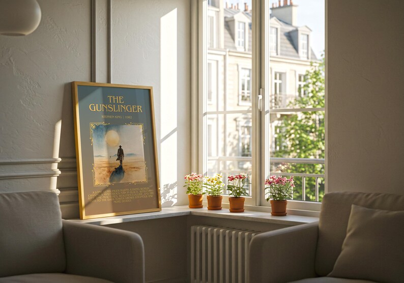 May include: A framed poster titled "The Gunslinger" leans against a wall next to a window. The poster features a figure on a beach with a large sun. Small potted plants sit on the windowsill. Two armchairs are in the foreground.