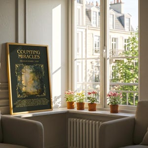May include: A framed art print titled "Counting Miracles" with a forest scene, displayed near a window with potted flowers. The print has a gold frame and is set against a neutral-toned wall. Two armchairs are in the foreground.