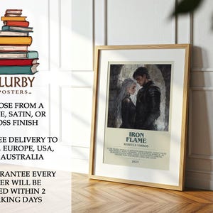 May include: A framed poster featuring a couple from the book "Iron Flame" by Rebecca Yarros. The artwork depicts a man and woman in dark attire, set against a stone background. The poster is in a wooden frame and is displayed on a wooden surface.
