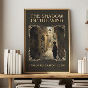 May include: A framed book cover for "The Shadow of the Wind" by Carlos Ruiz Zafón. The artwork depicts a boy standing in a narrow, stone-walled alleyway lit by a lantern. The title and author's name are in gold lettering.