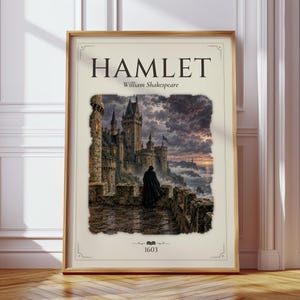 Op de afbeelding: Een ingelijste poster met de titel HAMLET en de auteur William Shakespeare. De centrale illustratie toont een donker stenen kasteel op een klif bij zonsondergang met een figuur in een mantel op een balkon. De tekst 1603 staat onderaan.