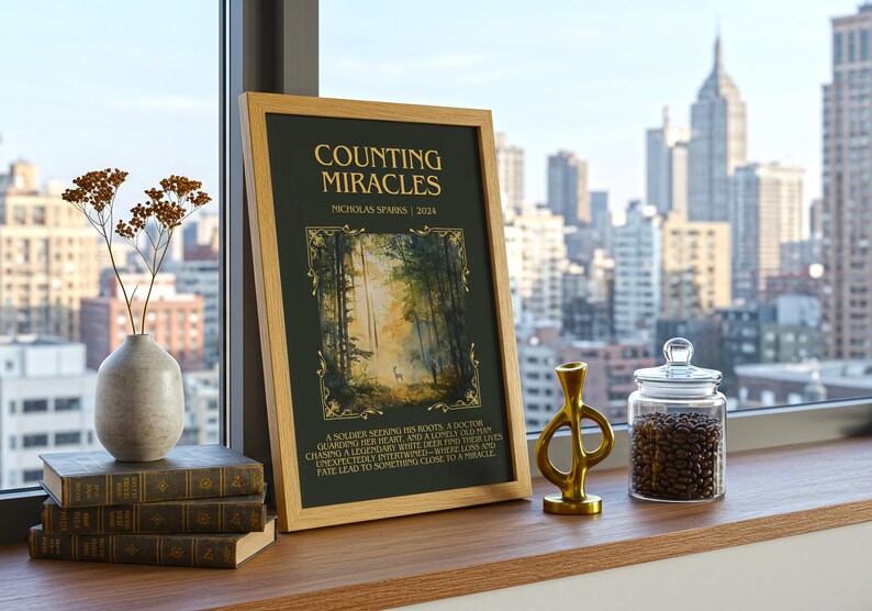 May include: A framed print titled "Counting Miracles" by Nicholas Sparks, displayed on a wooden surface. The print features a forest scene and text. Beside it are books, a vase with dried flowers, a gold sculpture, and a glass jar filled with coffee beans.