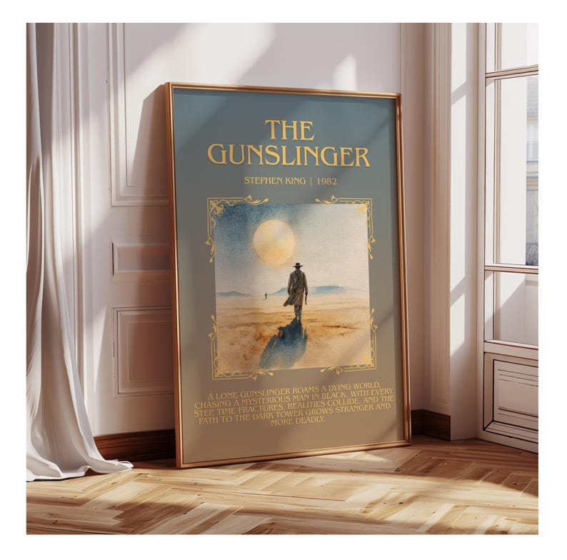 May include: A framed art print of "The Gunslinger" by Stephen King. The artwork depicts a desert landscape with a lone figure, a large moon, and gold text. The frame is gold, and the colour scheme is muted, giving a vintage feel.