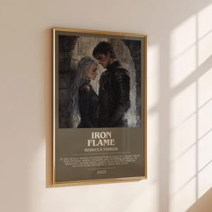 May include: A framed poster with a gold border hangs on a beige wall. The poster features a grayscale illustration of two people in a romantic embrace. The text "IRON FLAME" and "REBECCA YARROS" are visible, along with additional text and the year "2023".