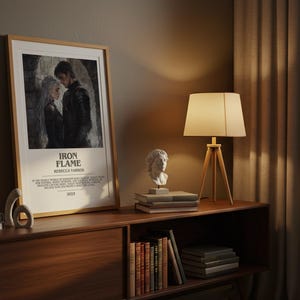 May include: A framed poster with the text "IRON FLAME" and an image of two people. The poster is displayed on a wooden cabinet with a lamp and two white busts. Books and decorative objects are also on the cabinet.