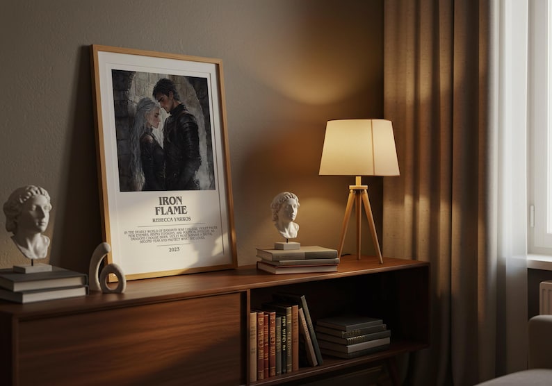 May include: A framed poster with the text "IRON FLAME" and an image of two people. The poster is displayed on a wooden cabinet with a lamp and two white busts. Books and decorative objects are also on the cabinet.