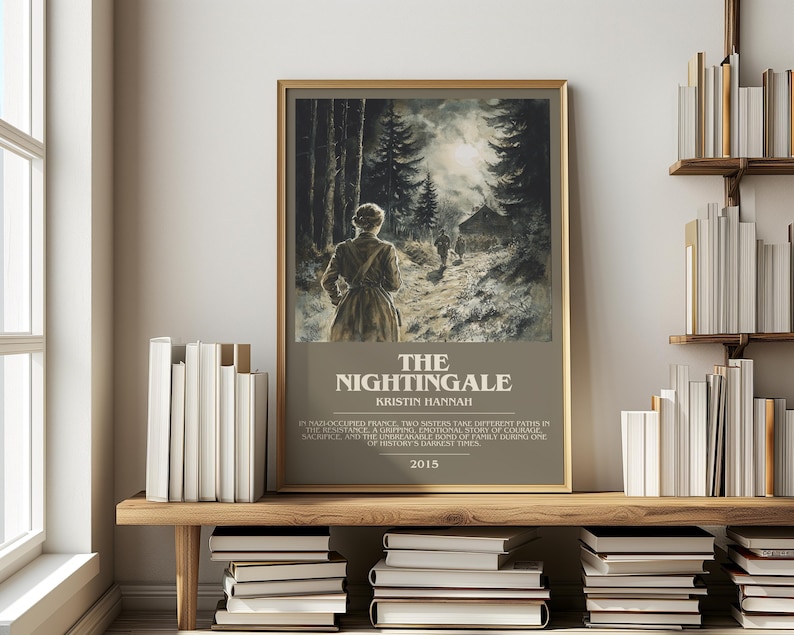 May include: A framed print of "The Nightingale" by Kristin Hannah, featuring a woman walking on a path through a forest. The print has a gold frame and is displayed on a wooden shelf with books.