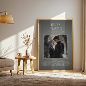 May include: A framed print with the title "IRON FLAME" and an illustration of a couple. The print is displayed in a room with a beige armchair, a side table, and a floor lamp. The room has a neutral color palette.