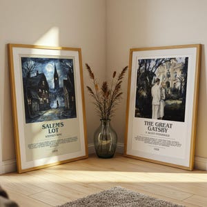 May include: Two framed movie posters, one for "Salem's Lot" and the other for "The Great Gatsby," lean against a wall. The "Salem's Lot" poster depicts a spooky town scene. The "Great Gatsby" poster shows a couple in front of a mansion. Both are in wooden frames.