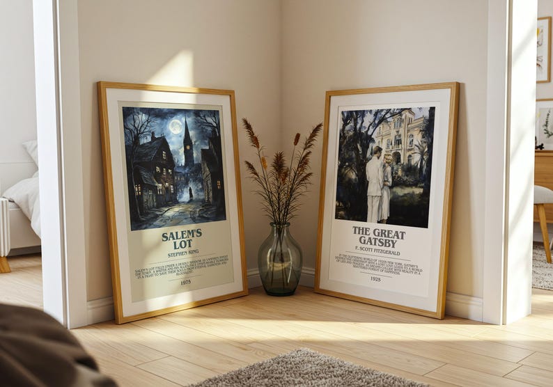 May include: Two framed movie posters, one for "Salem's Lot" and the other for "The Great Gatsby," lean against a wall. The "Salem's Lot" poster depicts a spooky town scene. The "Great Gatsby" poster shows a couple in front of a mansion. Both are in wooden frames.
