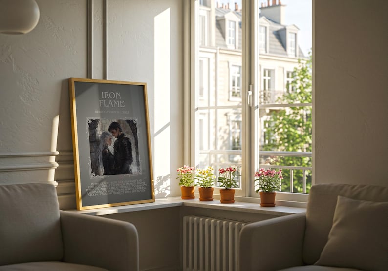 May include: A framed poster with the text "IRON FLAME" and an image of a couple. The poster is leaning against a wall next to a window with potted plants. Two armchairs are in the foreground.