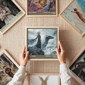 May include: A collection of framed art prints featuring book covers and illustrations. One print shows a woman with a dragon, with the text "TX-STORM" and "REBECCA YARROS 2023". Other prints include "CHARLOTTES WEB", "LITTLE WOMEN", and "EVIL UNDER THE SUN".