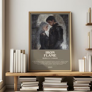 May include: A framed print of "Iron Flame" by Rebecca Yarros, featuring a couple in medieval attire. The print has a gold frame and is displayed on a wooden shelf with books. The text "Iron Flame" and the author's name are visible.