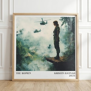 May include: Framed print featuring a woman in military attire standing on a wooden platform, with helicopters flying overhead. The artwork has a jungle backdrop with tents and smoke. Text at the bottom reads "THE WOMEN" and "KRISTIN HANNAH 2024".