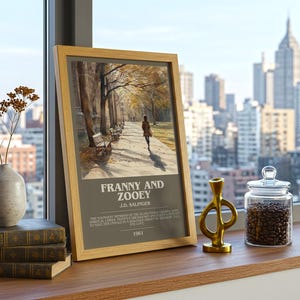 K&ouml;nnte beinhalten: Ein gerahmter Druck einer Person, die auf einem Weg mit B&auml;nken, B&auml;umen und Herbstlaub geht. Der Druck tr&auml;gt den Titel "Franny and Zooey" von J.D. Salinger, mit Text darunter. Eine Vase mit getrockneten Blumen, B&uuml;cher, eine goldene Skulptur und ein Glas mit Kaffeebohnen stehen auf einer Holzoberfl&auml;che.