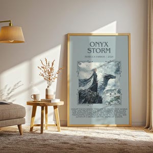 May include: A framed poster with the title "ONYX STORM" and the name "REZZCCA YARBOS | 2025". The artwork depicts a woman and a dragon on a rocky landscape, with text below. The frame is gold.