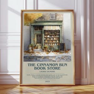 Könnte beinhalten: Ein gerahmter Kunstdruck mit einer Aquarellillustration einer Buchhandlung mit grünen Rahmen, Bücherregalen und Herbstlaub. Der Text lautet THE CINNAMON BUN BOOK STORE, LAURIE GILMORE, sowie eine Zusammenfassung der Geschichte, datiert 2023.