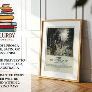 May include: A framed poster of "The Nightingale" by Kristin Hannah, featuring a woman walking in a forest. The poster is in a light wood frame, leaning against a white wall. The poster is on a wooden floor.