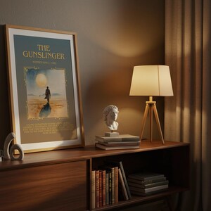 May include: A framed poster titled "The Gunslinger" with a desert scene illustration. It's displayed on a wooden cabinet with a lamp, books, and a bust. The scene is lit by a warm, ambient light.