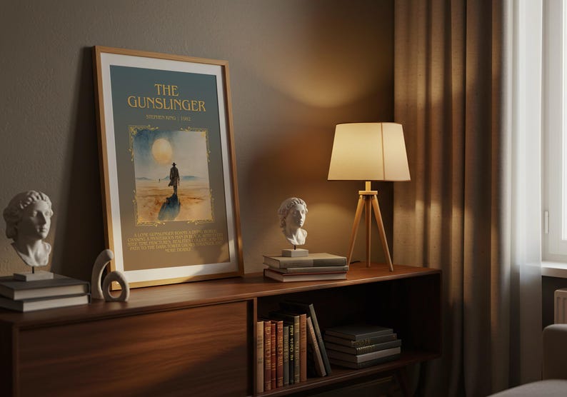 May include: A framed poster titled "The Gunslinger" with a desert scene illustration. It's displayed on a wooden cabinet with a lamp, books, and a bust. The scene is lit by a warm, ambient light.