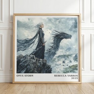 May include: A framed print featuring a woman with long white hair and a dark gown standing on a rocky cliff, with a dragon in the background. The artwork is in shades of gray and blue, with the text "ONYX STORM" and "REBECCA YARROS 2025" at the bottom.