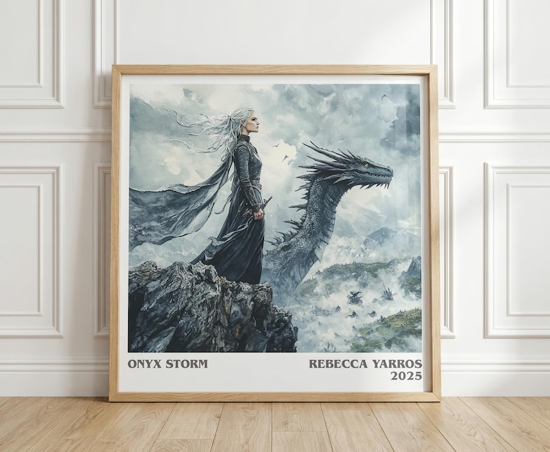 May include: A framed print featuring a woman with long white hair and a dark gown standing on a rocky cliff, with a dragon in the background. The artwork is in shades of gray and blue, with the text "ONYX STORM" and "REBECCA YARROS 2025" at the bottom.