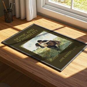 May include: Framed print of "Sense and Sensibility" by Jane Austen, 1811. The artwork depicts a couple embracing on a grassy hill. The frame is silver, and the background is a dark olive green.