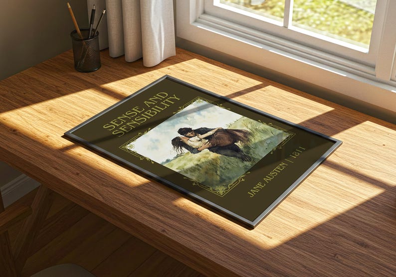 May include: Framed print of "Sense and Sensibility" by Jane Austen, 1811. The artwork depicts a couple embracing on a grassy hill. The frame is silver, and the background is a dark olive green.