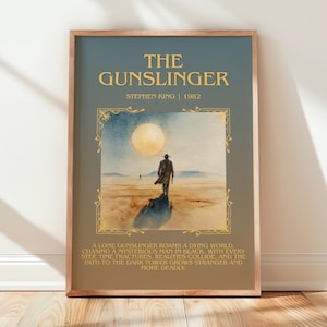 May include: Framed art print of "The Gunslinger" by Stephen King. The artwork depicts a lone figure walking towards a large moon in a desert landscape. The title and author's name are displayed in gold lettering.