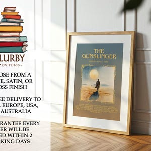 May include: A framed poster of "The Gunslinger" book cover art by Stephen King. The image shows a figure on a beach under a large moon. The poster is in a wooden frame and is leaning against a wall. The poster is part of a series.
