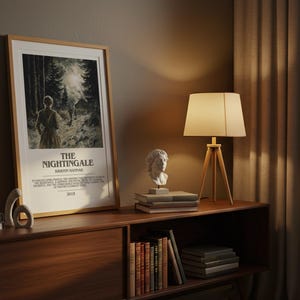 May include: A framed poster for "The Nightingale" movie, featuring a forest scene and the title text. The poster is displayed on a wooden cabinet with a lamp, books, and a bust sculpture. The room has a warm, inviting atmosphere.