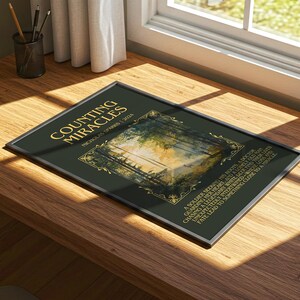 May include: A framed art print titled "Counting Miracles" by Nicholas Sparks. The print features a dark green background with gold lettering and a landscape image. The frame is silver.