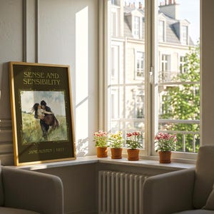 May include: A framed print of "Sense and Sensibility" by Jane Austen, featuring a romantic illustration of a couple. The print is displayed near a window with potted plants, creating a cozy, literary atmosphere. The frame is gold.
