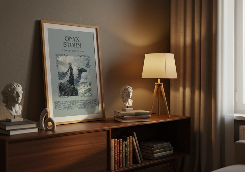 May include: A framed art print titled "Onyx Storm" with a fantasy illustration, displayed on a wooden cabinet. The scene includes a bust, a lamp, and books, creating a cozy, artistic atmosphere. The print is in a light blue frame.