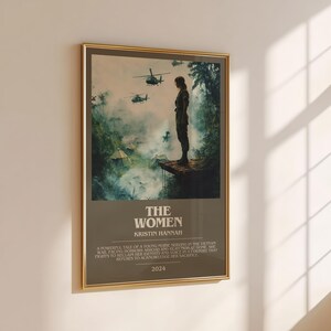 Puede incluir: Un p&oacute;ster enmarcado con borde dorado, que muestra a una mujer de pie en una plataforma con helic&oacute;pteros al fondo. El p&oacute;ster tiene el t&iacute;tulo "THE WOMEN", el nombre de la autora, Kristin Hannah, texto y el a&ntilde;o 2024.