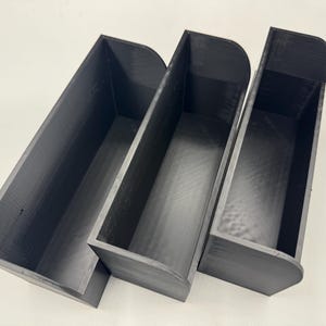 Op de afbeelding: Drie zwarte, wandgemonteerde opbergcontainers van plastic met afgeronde randen. De containers zijn op elkaar gestapeld.