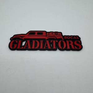 May include: Red and black logo with the text "GLADIATORS" and "SOCAL" featuring a red silhouette of a pickup truck with a camper shell.