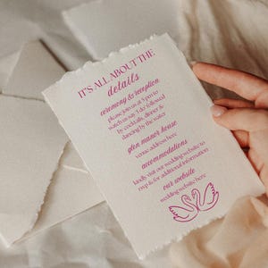 May include: A textured, off-white wedding invitation with torn edges. The invitation features magenta text that reads "IT'S ALL ABOUT THE details" and wedding details. A pair of swans is printed at the bottom.