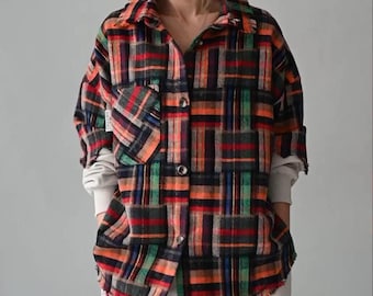 May include: A colorful plaid shirt with a patchwork design in shades of red, orange, green, and black. The shirt has a button-down front, a chest pocket, and long sleeves. The person is wearing light-colored pants.