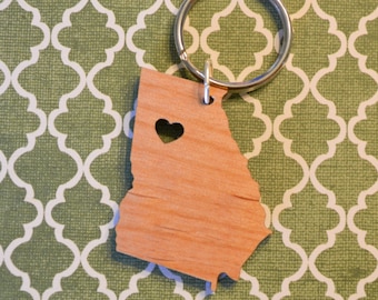 May include: A wooden keychain shaped like the state of Georgia with a small heart cutout in the center. The keychain is attached to a silver key ring.